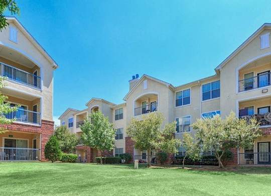 Apartment complex with green lawn and trees at Addison Park Apartments in Arlington, TX.