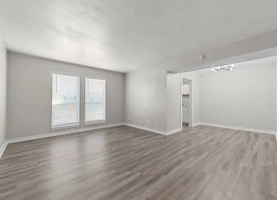 A spacious room with wooden flooring and two windows.
