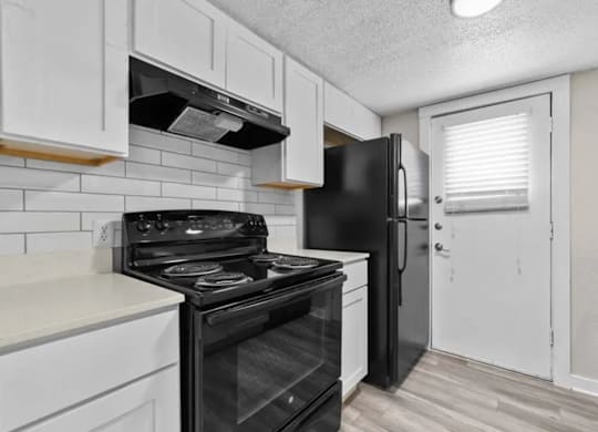 A black refrigerator sits in a kitchen with white cabinets.