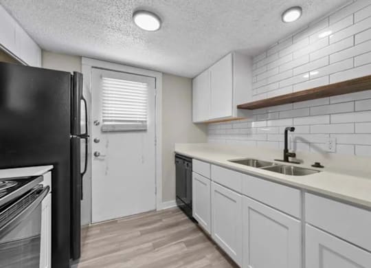 A kitchen with white cabinets and a black refrigerator.