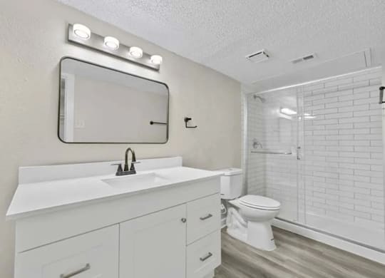 A white bathroom with a sink, mirror, and toilet.