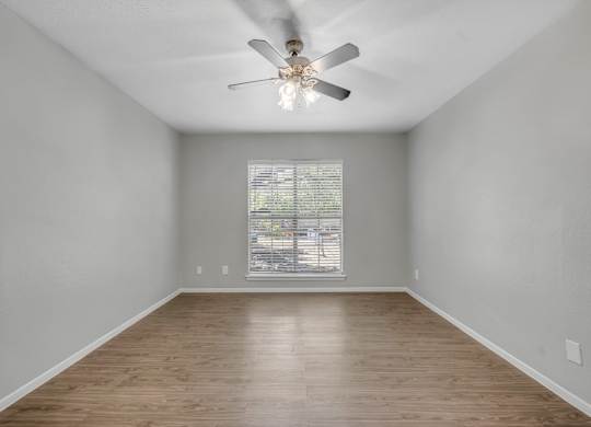 A room with a ceiling fan and wooden flooring.