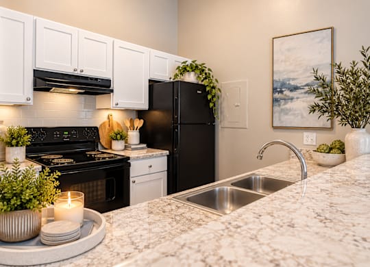 A modern kitchen with a black refrigerator and white cabinets.