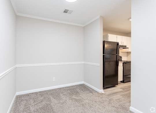 an empty room with white walls and a kitchen with a black refrigerator