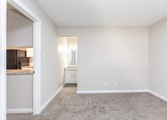 an empty living room with carpet and a kitchen