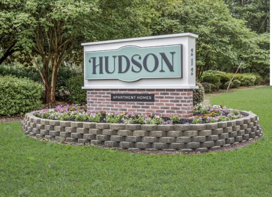 The sign for Hudson Apartments in a grass field and trees