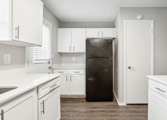 an empty kitchen with white cabinets and a black refrigerator