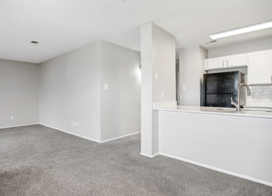 the living room and kitchen of an apartment with white walls and carpet