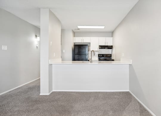 the living room and kitchen of an apartment with white walls and carpeted flooring