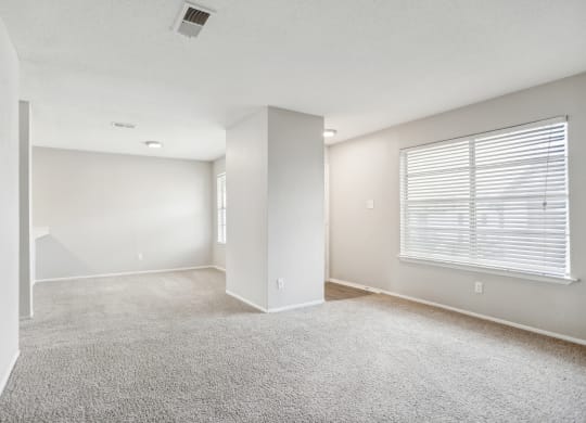 the spacious living room and dining room of an apartment with white walls and carpet