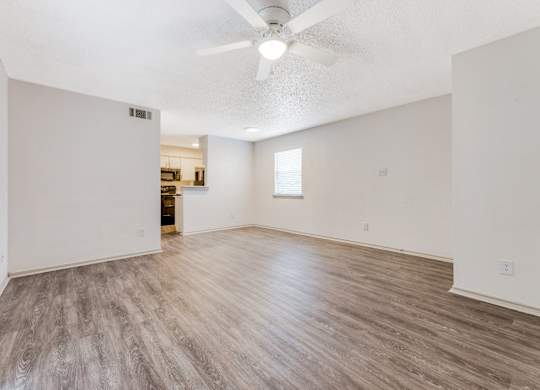 an empty living room with a ceiling fan and a kitchen