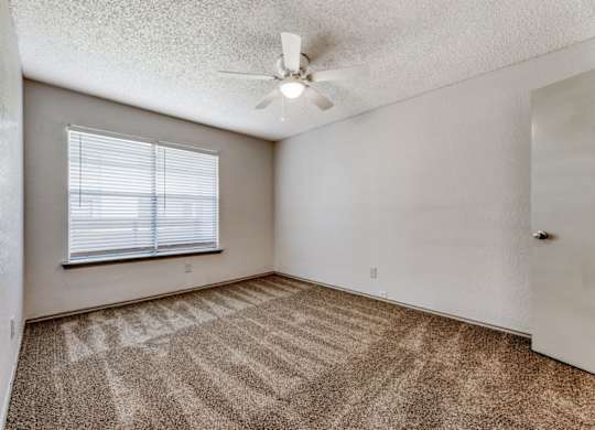 an empty bedroom with a ceiling fan and a window