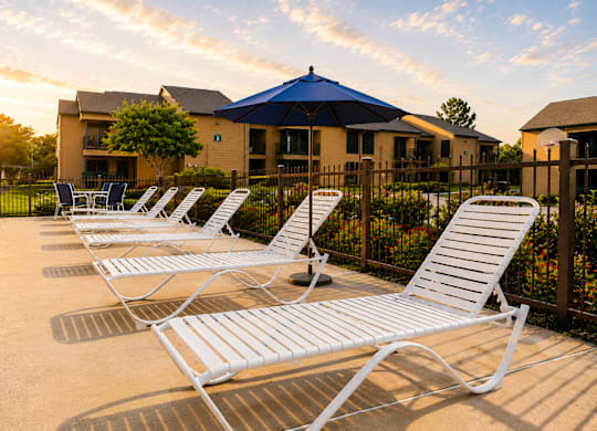 Pool deck with white lounge chairs and blue umbrella at Ridgeview Apartments, Sherman, TX