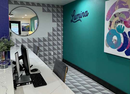 A white desk with a computer on it in front of a green wall with a Lumina logo.
