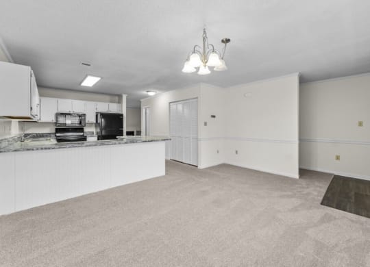 an empty living room and kitchen with white cabinets and a counter top