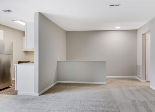 an empty living room with a kitchen and a stainless steel refrigerator