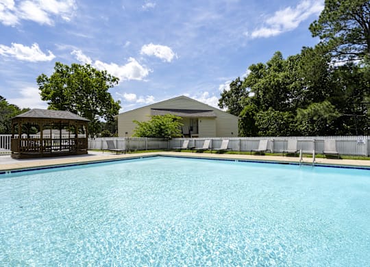 A large swimming pool in front of a house with a gazebo.