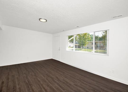 an empty living room with wood floors and a window