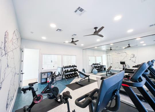 a gym with treadmills and other exercise equipment in a room with windows