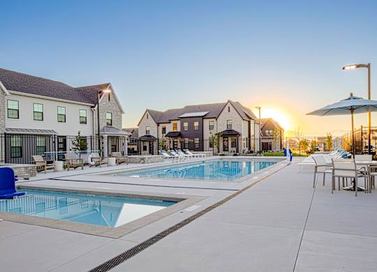 A sunset view of a pool area with lounge chairs and umbrellas.
