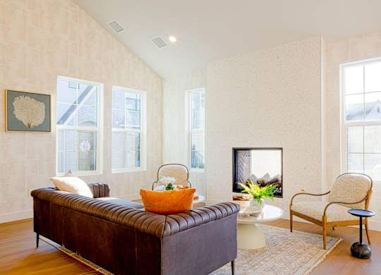 A living room with a brown leather couch, a white side table, and a chair.
