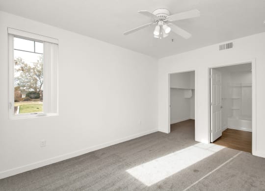 an empty bedroom with a ceiling fan and a door to a bathroom