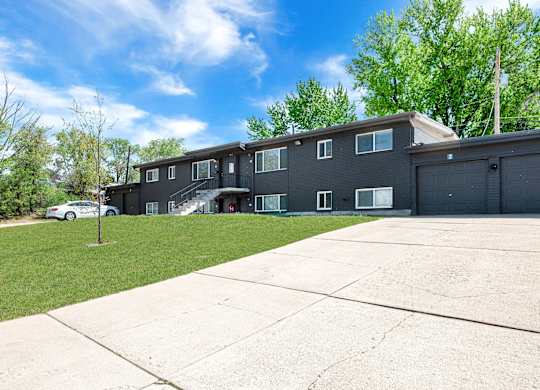 the front of an apartment building with a driveway and lawn