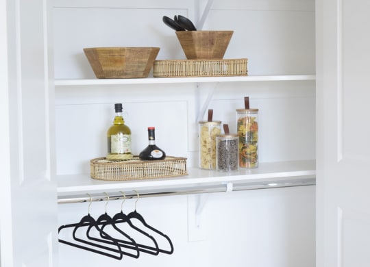 a white pantry with baskets on the top of the shelves and black hangers on the