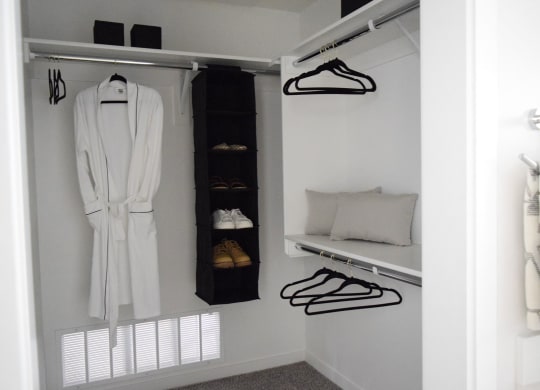 a walk in closet with a white robe and a shelf with shoes and a pillow