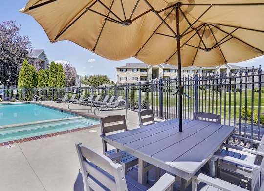 A table with chairs and an umbrella is set up by a pool.