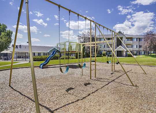A playground with swings and a slide in front of a building.