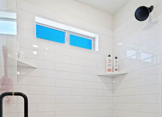 a white tiled bathroom with a shower and a window