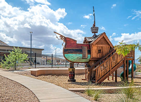 A playground with a wooden pirate ship structure and a green slide.