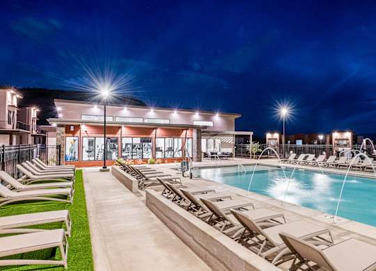 A poolside area with lounge chairs and a building in the background.