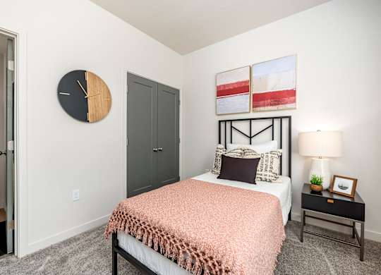 A bedroom with a bed, nightstand, and a clock on the wall.