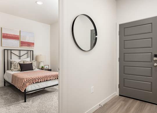 A bedroom with a bed, pillows, a round mirror, and a grey door.