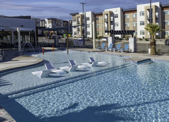a resort style pool with white lounge chairs in it with an apartment building behind it