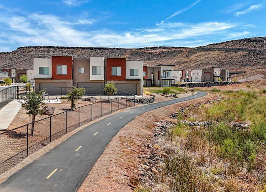 A road with a fence on the side and houses in the background.
