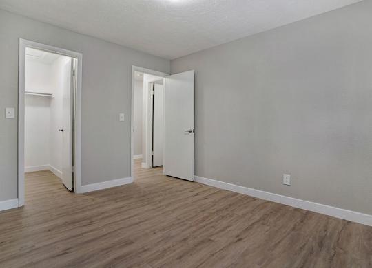 A room with white walls and wooden flooring with three open doors.