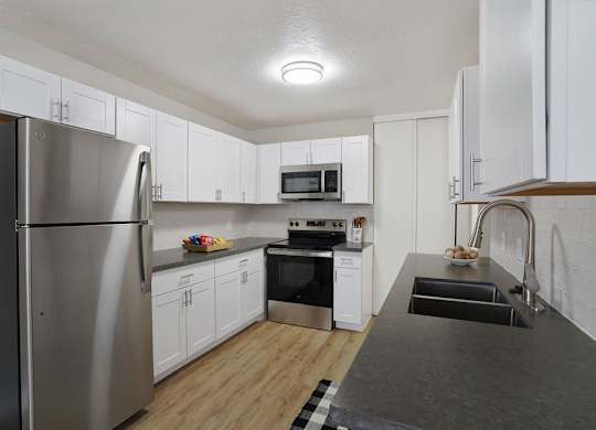 A kitchen with a refrigerator, oven, microwave, and sink.