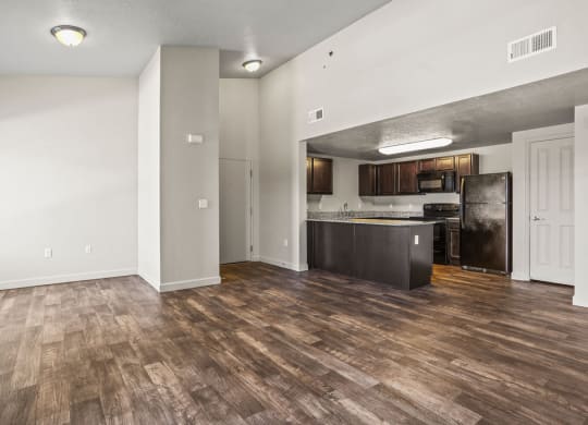 an empty living room with a kitchen with a refrigerator