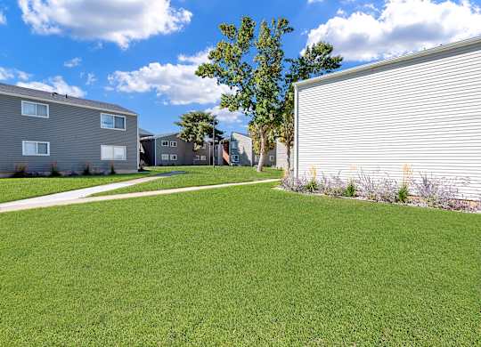 A grassy area in front of a building with a tree in the background.
