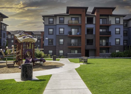 a pathway leading to an apartment building with a playground in the foreground
