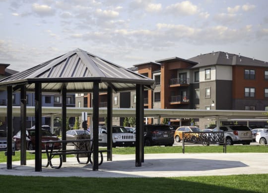 a gazebo in a park with apartment buildings in the background