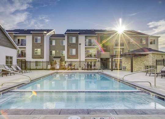 A swimming pool in front of a building with sunlight shining through the clouds.