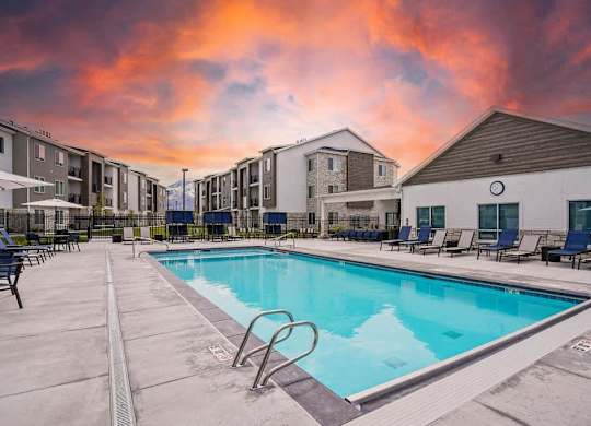 A swimming pool surrounded by lounge chairs and apartment buildings.