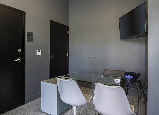 A black door is on the left of a room with a glass table and two white chairs.