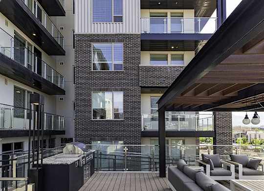 A modern balcony with a table and chairs is attached to a brick building.