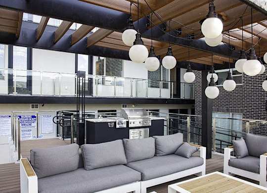 A modern outdoor seating area with grey couches and wooden tables.