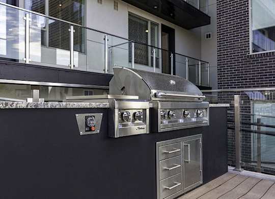 A stainless steel outdoor grill with a side burner and a drawer is on a black countertop.
